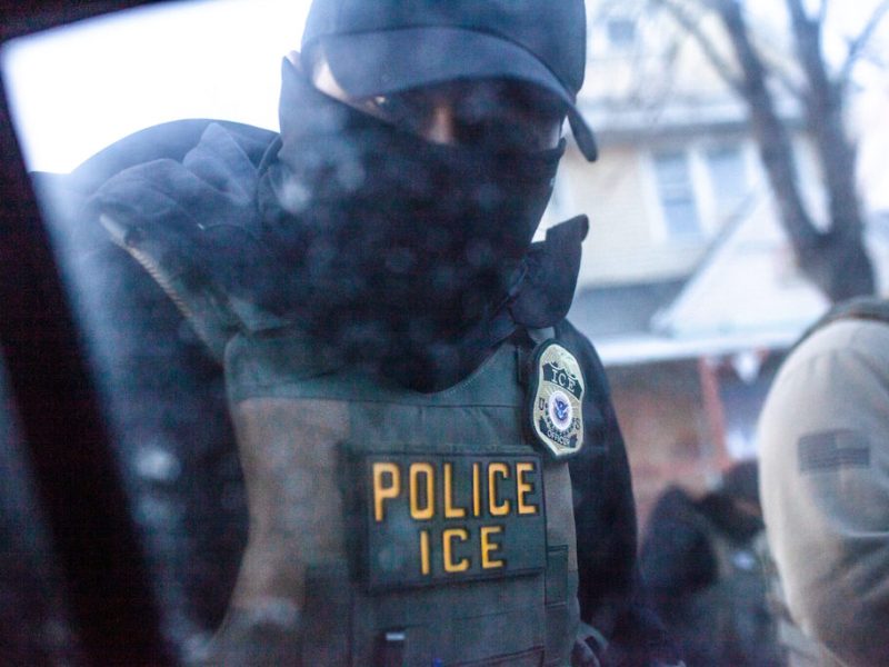 An ICE officer in a mask and hat.